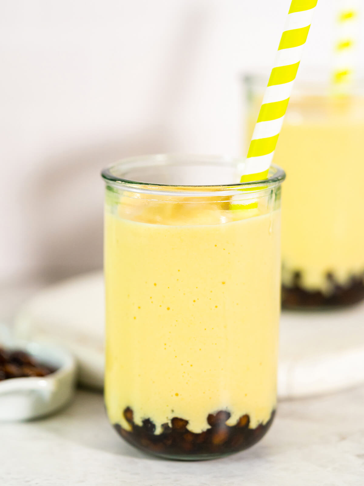 Cremiger Mango-Boba-Smoothie in hohem Glas mit Tapioka-Perlen am Boden und breitem Strohhalm