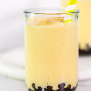 Cremiger Mango-Boba-Smoothie im hohen Glas mit Tapioka-Perlen am Boden und breitem Strohhalm