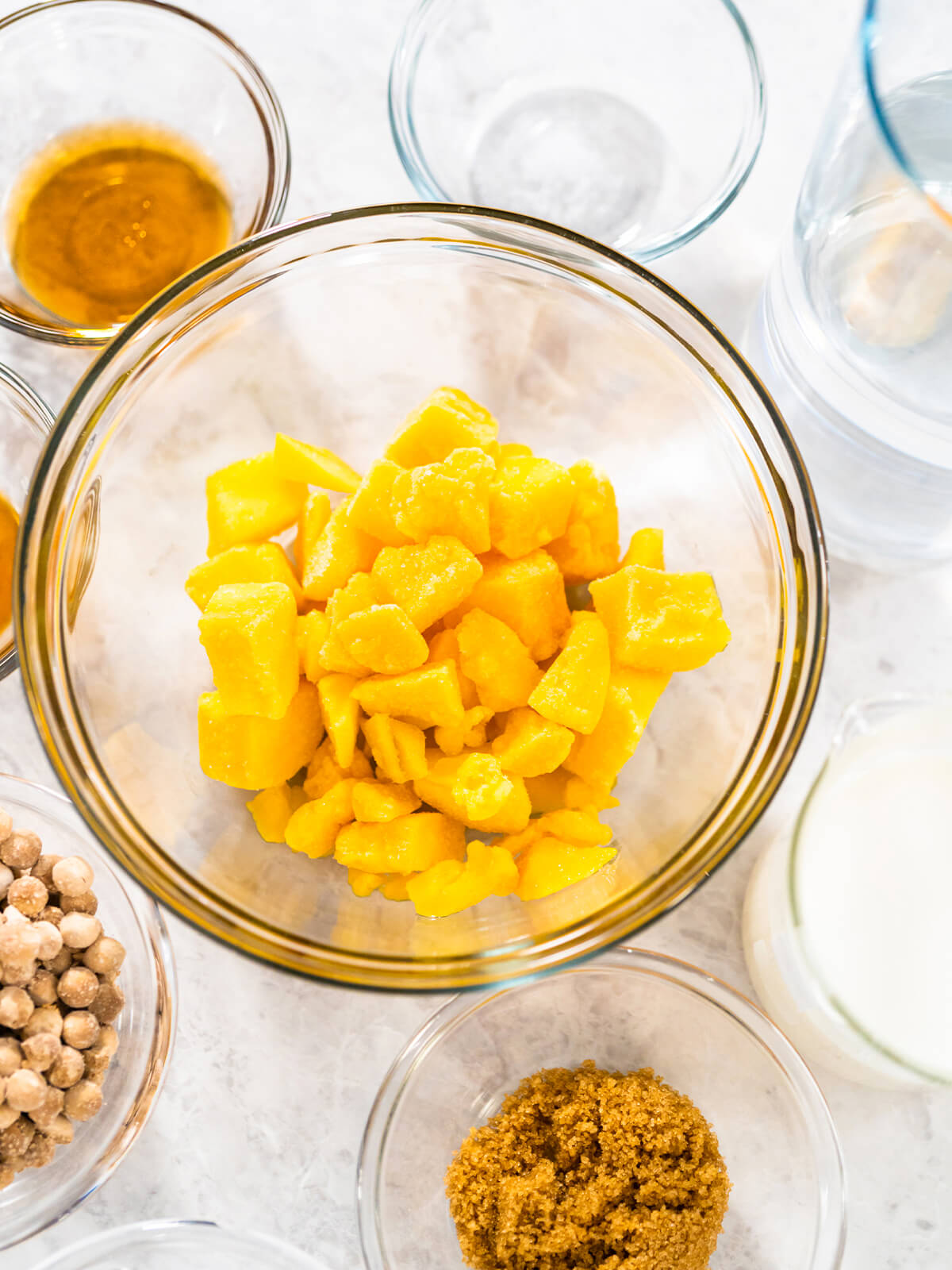 Zutaten für den Mango-Boba-Smoothie von oben – gefrorene Mango-Würfel, Milch, Vanille, brauner Zucker und trockene Boba-Perlen in Glasschälchen