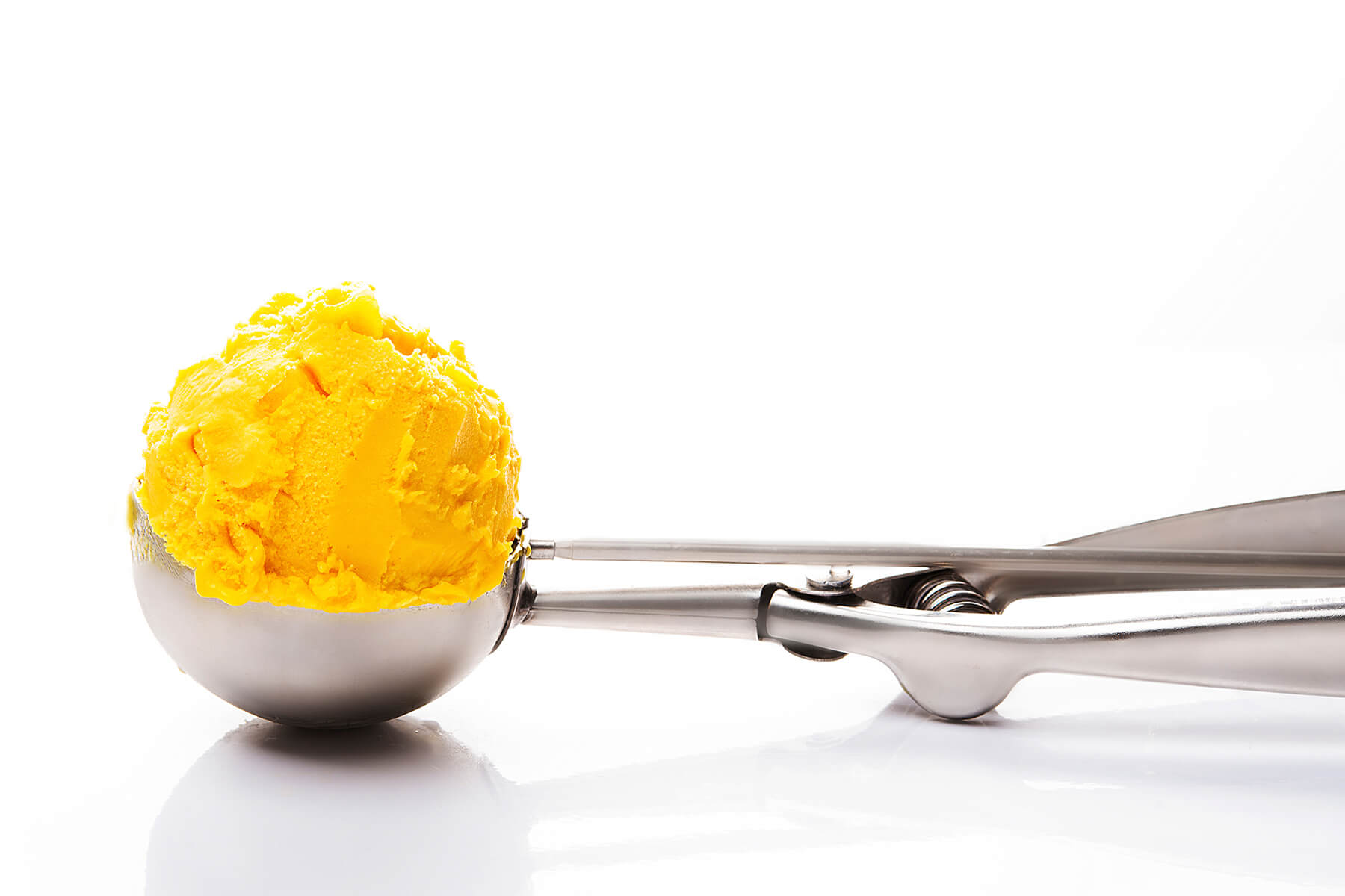 Cremige Mango-Sorbet-Kugel in einem Eisportionierer auf hellem Hintergrund