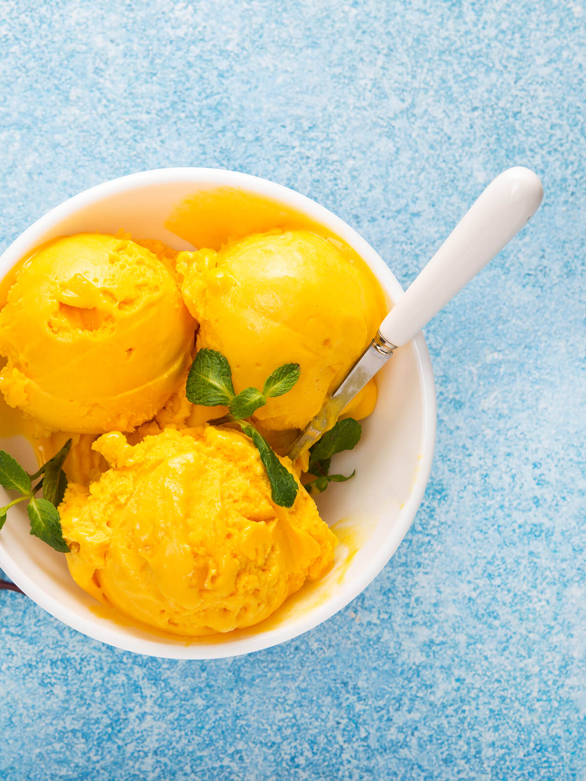 Mango-Sorbet-Kugeln in einer weißen Schale mit frischer Minze garniert