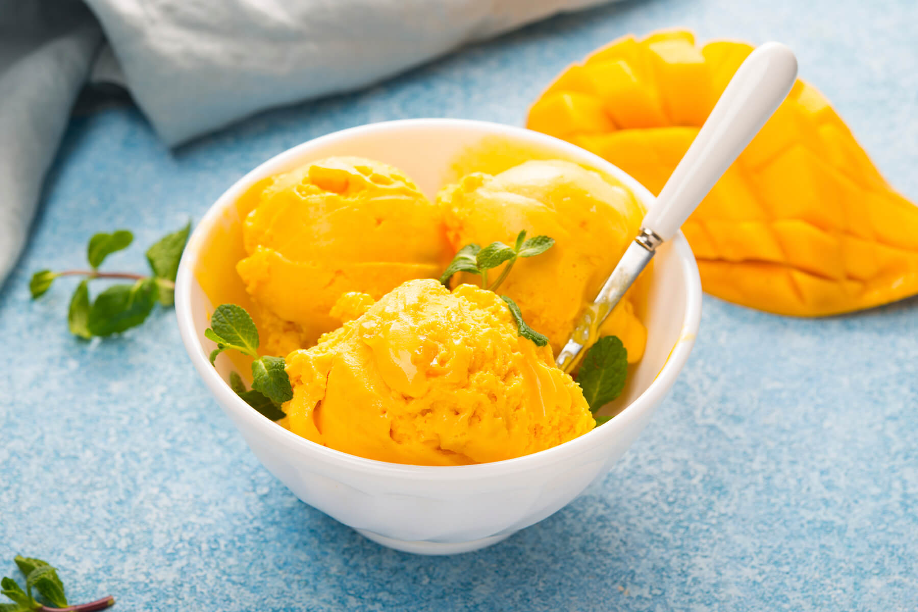 Schale mit Mango-Sorbet, frischer Minze und einer aufgeschnittenen Mango daneben