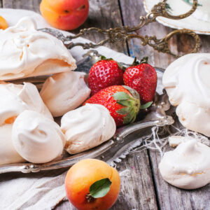 Klassische französische Meringue in drei Größen auf einem Silbertablett mit Erdbeeren und Aprikosen