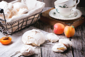 Französische Meringue im mit Leinen ausgelegten Drahtkorb, daneben ganze und halbierte Aprikosen