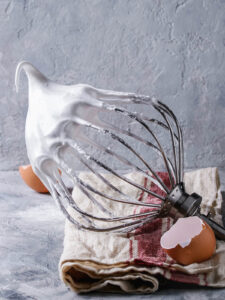 Aufgeschlagene Meringue-Masse hängt in einem langen weichen Haken am Schneebesen
