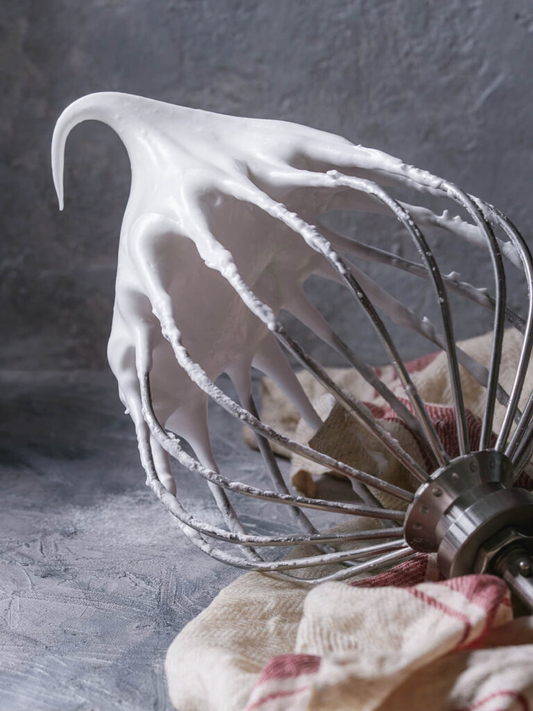Dichte, glänzende Meringue am waagerecht gehaltenen Schneebesen, die Spitze steht und biegt sich vorne leicht um