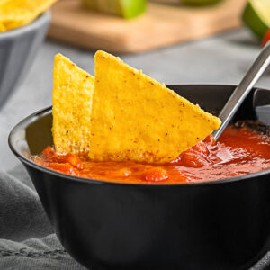 Mexikanischer Tomaten-Dip in dunkler Schale mit Tortilla-Chips