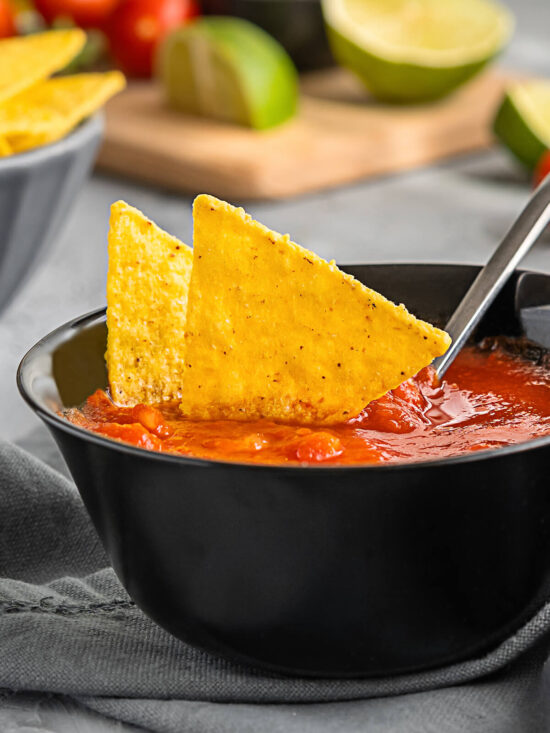Mexikanischer Tomaten-Dip in dunkler Schale mit Tortilla-Chips