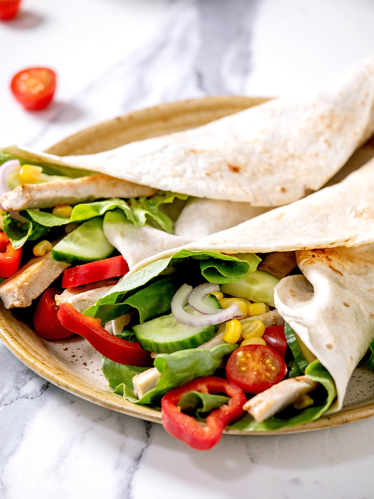 Nahaufnahme zweier locker übergeklappter Tortilla-Wraps mit Salat, Gurkenscheiben, roter Zwiebel, Mais, Cherry-Tomaten und Schweinefilet