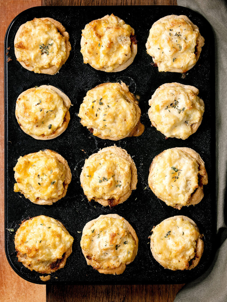 Zwölf Mini Cottage Pies mit goldener Cheddar-Kartoffelpüree-Haube auf dem Backblech von oben