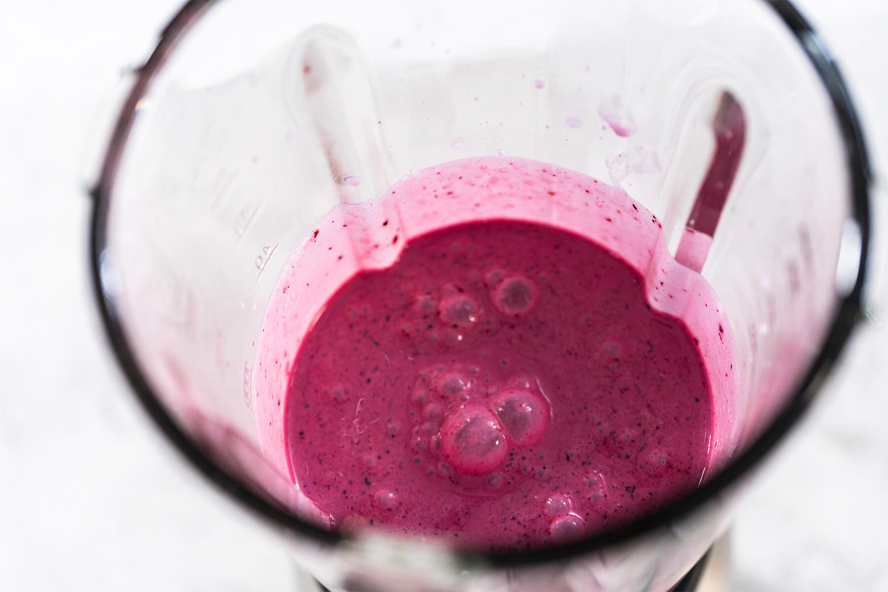 Aufsicht in den Standmixer auf den fertig pürierten, dunkel-violetten Beeren-Smoothie