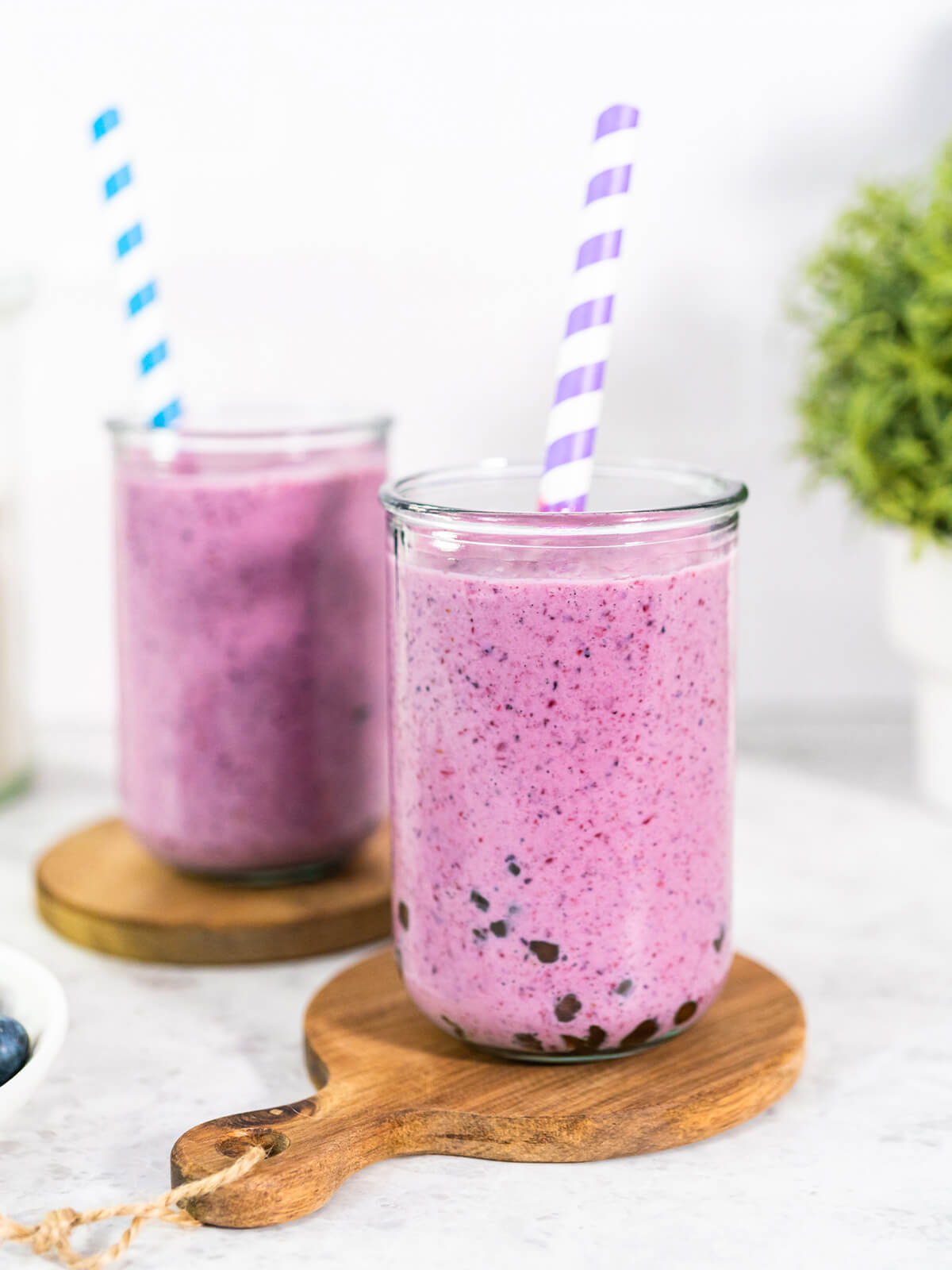 Zwei hohe Gläser Mixed-Berry-Boba-Smoothie mit dunklen Tapioka-Perlen am Boden und Papierstrohhalmen auf Holzbrettchen