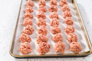 Backblech mit 28 roh portionierten Hackbällchen vor dem Backen von oben