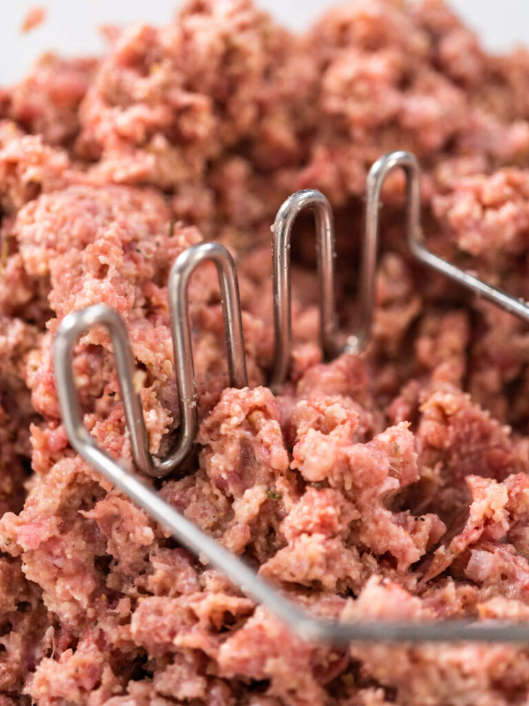 Hackmasse wird mit einem Kartoffelstampfer vermischt, Nahaufnahme