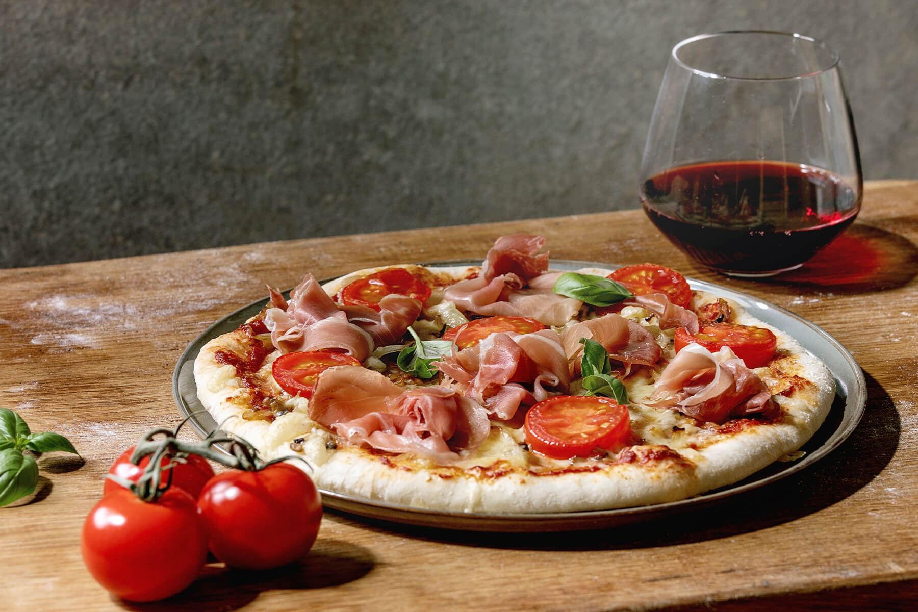 Pizza Napoletana mit Parmaschinken, halbierten Cocktailtomaten, Champignons und Basilikum auf grünem Teller