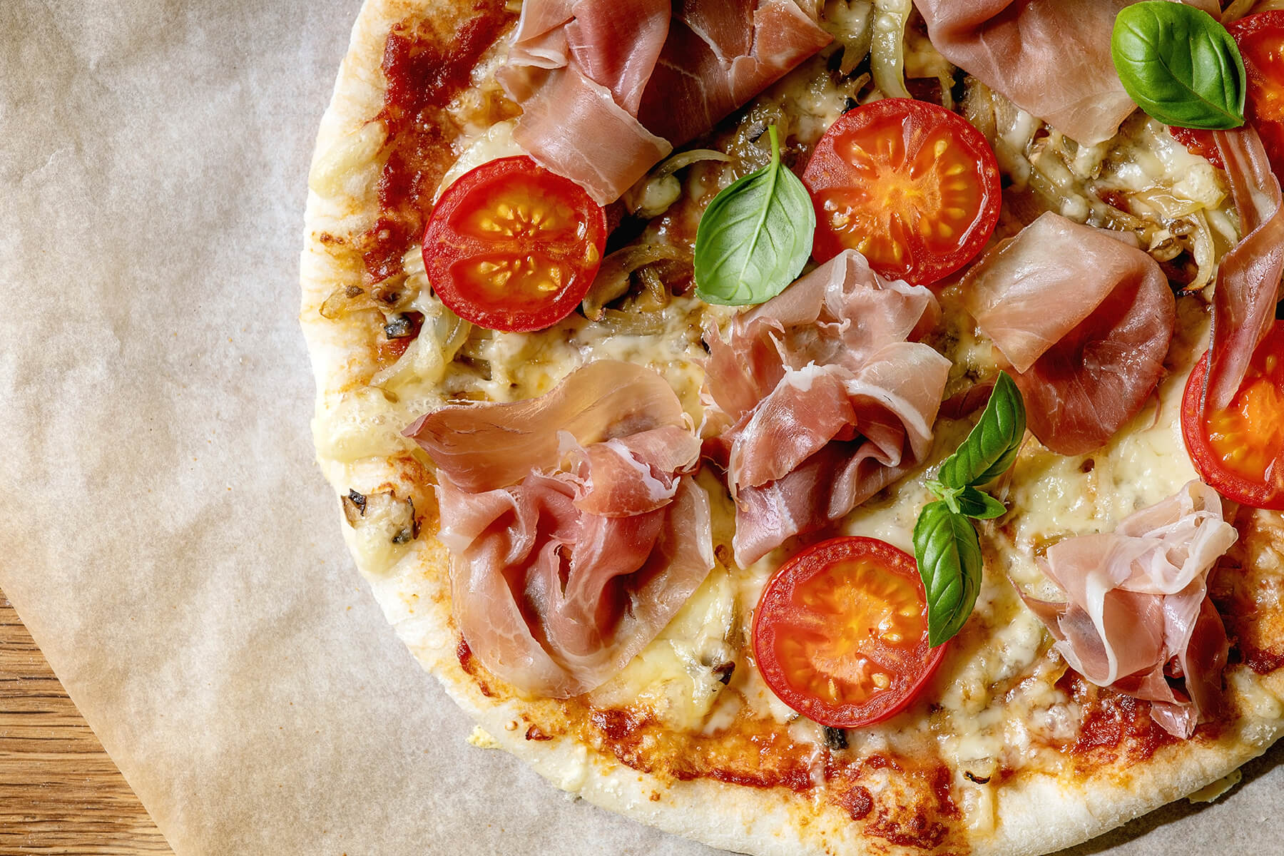 Nahaufnahme der Pizza Napoletana mit Parmaschinken, halbierten Cocktailtomaten, gebratenen Champignons und Basilikum
