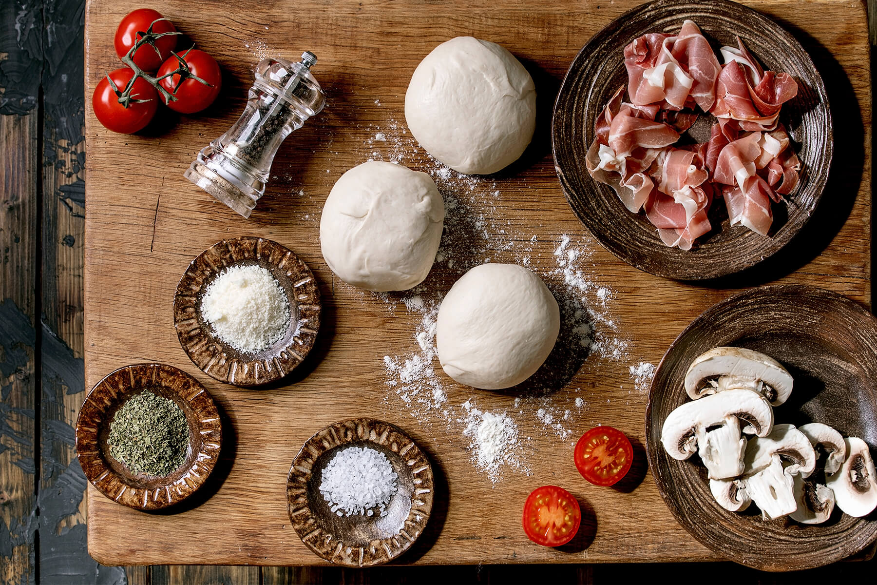 Mise en place mit Teigballen, Parmaschinken, Cocktailtomaten, geriebenem Käse und Champignons