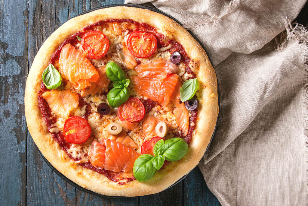 Pizza mit Tomatensauce, Mozzarella, Räucherlachs, Kirschtomaten und Oliven