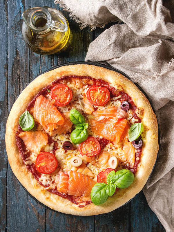 Pizza mit Tomatensauce, Mozzarella, Räucherlachs, Kirschtomaten, Oliven und Basilikum