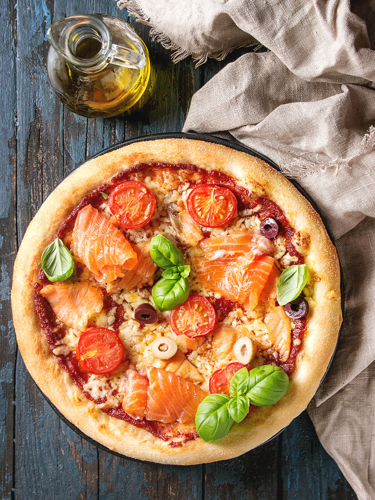 Pizza mit Tomatensauce, Mozzarella, Räucherlachs, Kirschtomaten, Oliven und Basilikum