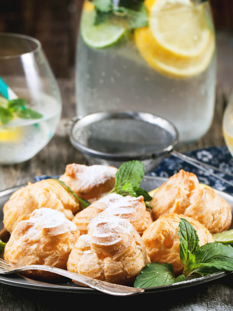 Profiteroles mit Puderzucker und Minze auf Metallplatte mit Zitronen-Limonade