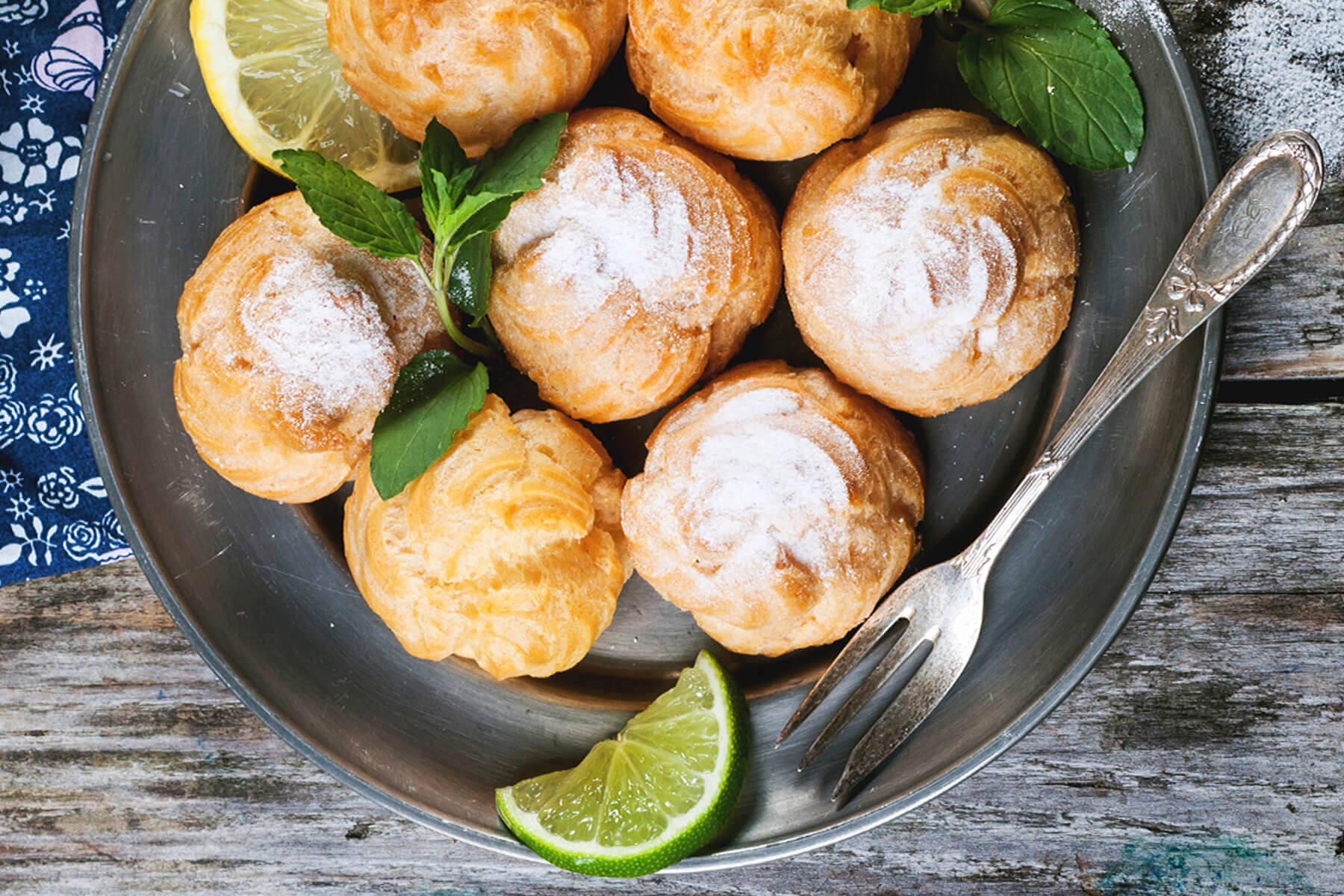 Profiteroles mit Puderzucker, Minze, Zitrone und Limette auf einer Metallplatte