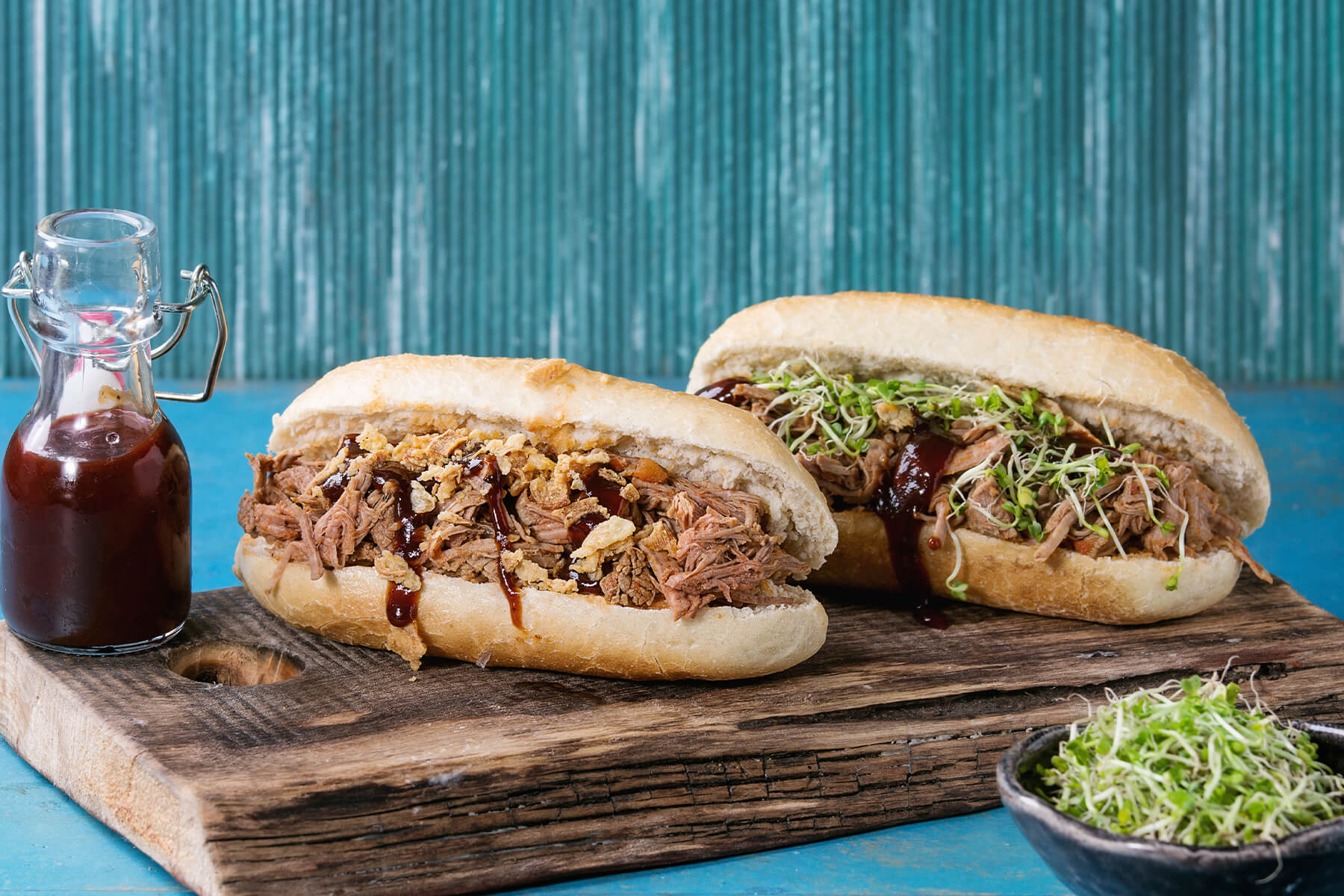 Zwei Pulled Pork Subs mit Röstzwiebeln und mit Sprossen auf Holzbrett