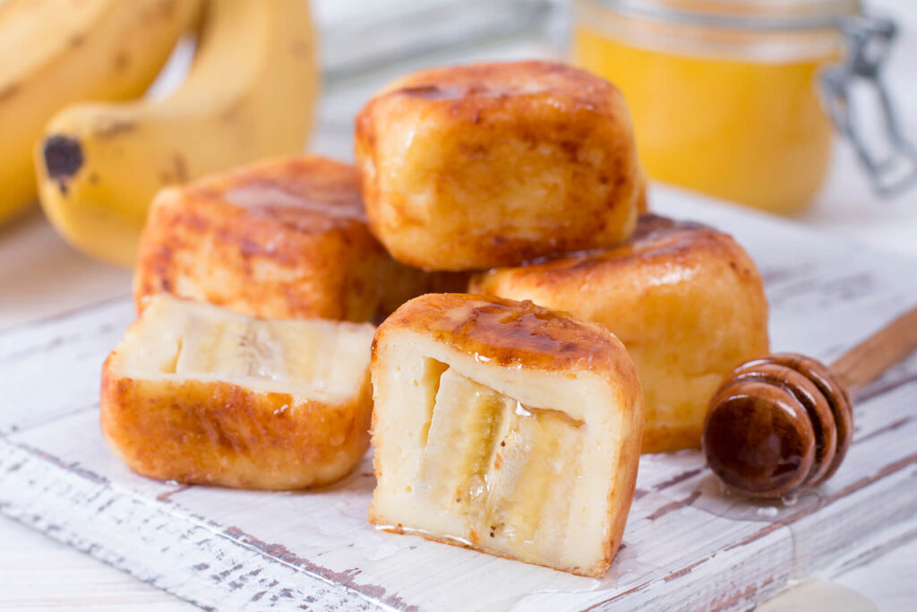 Aufgeschnittene Quark-Bananen-Würfel mit Bananenscheibe, beträufelt mit Honig vom Holzlöffel