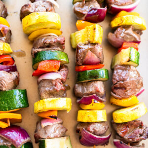 Bunte Rinder-Gemüse-Spieße mit grünen Zucchini-Scheiben, gelbem Sommerkürbis, roter und oranger Paprika und roten Zwiebeln