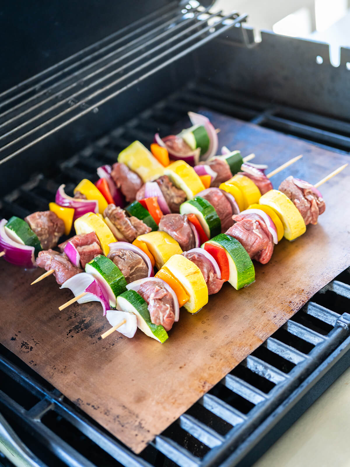 Rinder-Gemüse-Spieße auf einer Grillmatte über dem Gasgrill