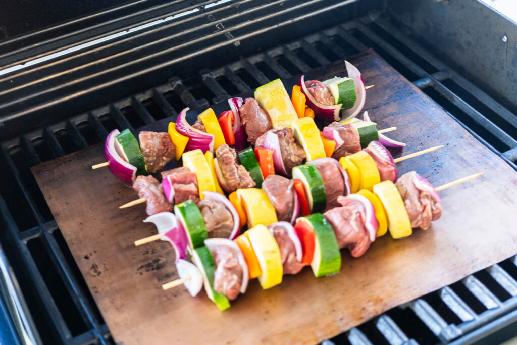 Rohe Rinder-Gemüse-Spieße auf der Grillmatte über dem vorgeheizten Gasgrill