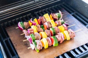 Rohe Rinder-Gemüse-Spieße auf der Grillmatte über dem vorgeheizten Gasgrill