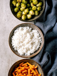 Gebackener Rosenkohl als Vegan-Bowl mit Reis und Babymöhren in drei Steingut-Schalen