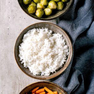 Gebackener Rosenkohl als Vegan-Bowl mit Reis und Babymöhren in drei Steingut-Schalen