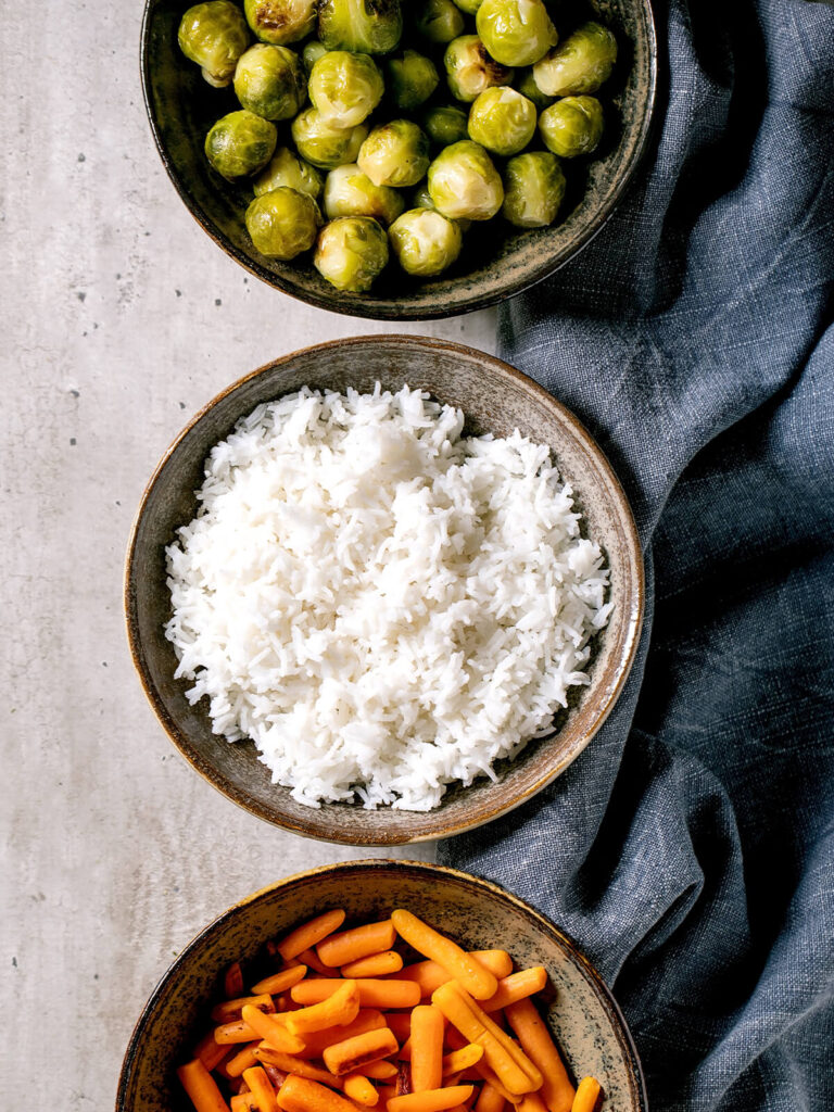 Gebackener Rosenkohl als Vegan-Bowl mit Reis und Babymöhren in drei Steingut-Schalen