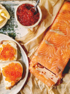 Lachs-Terrine mit zwei Broten, die mit rotem Kaviar belegt sind, und einer Schale Lachs-Kaviar