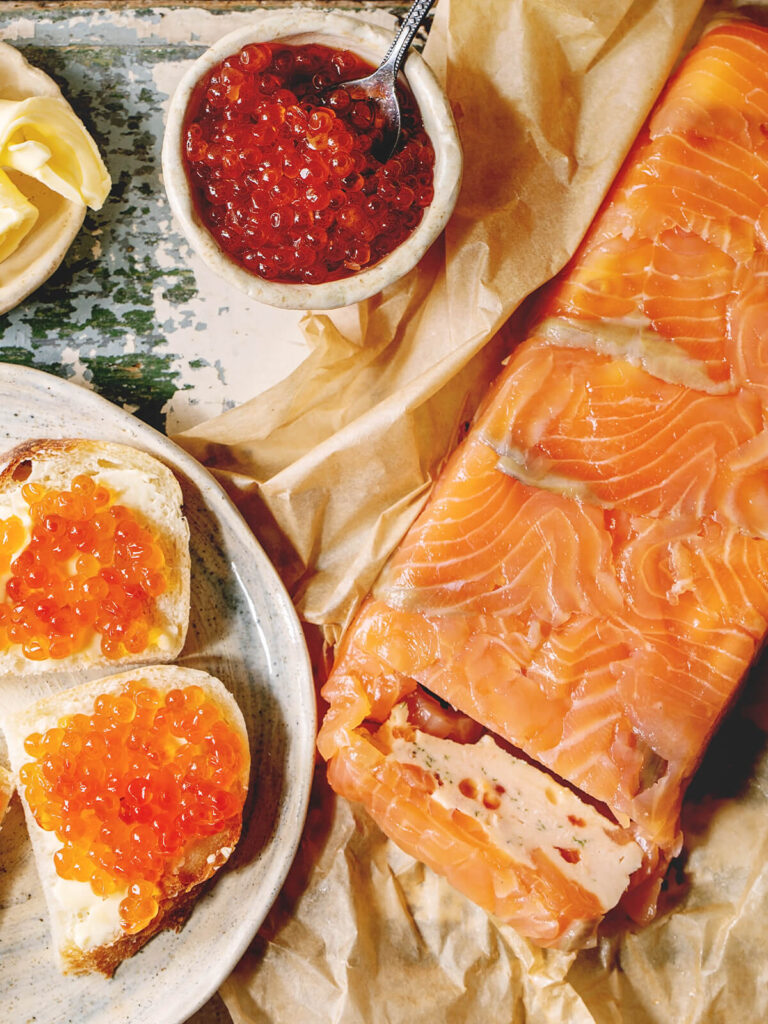 Lachs-Terrine mit zwei Broten, die mit rotem Kaviar belegt sind, und einer Schale Lachs-Kaviar