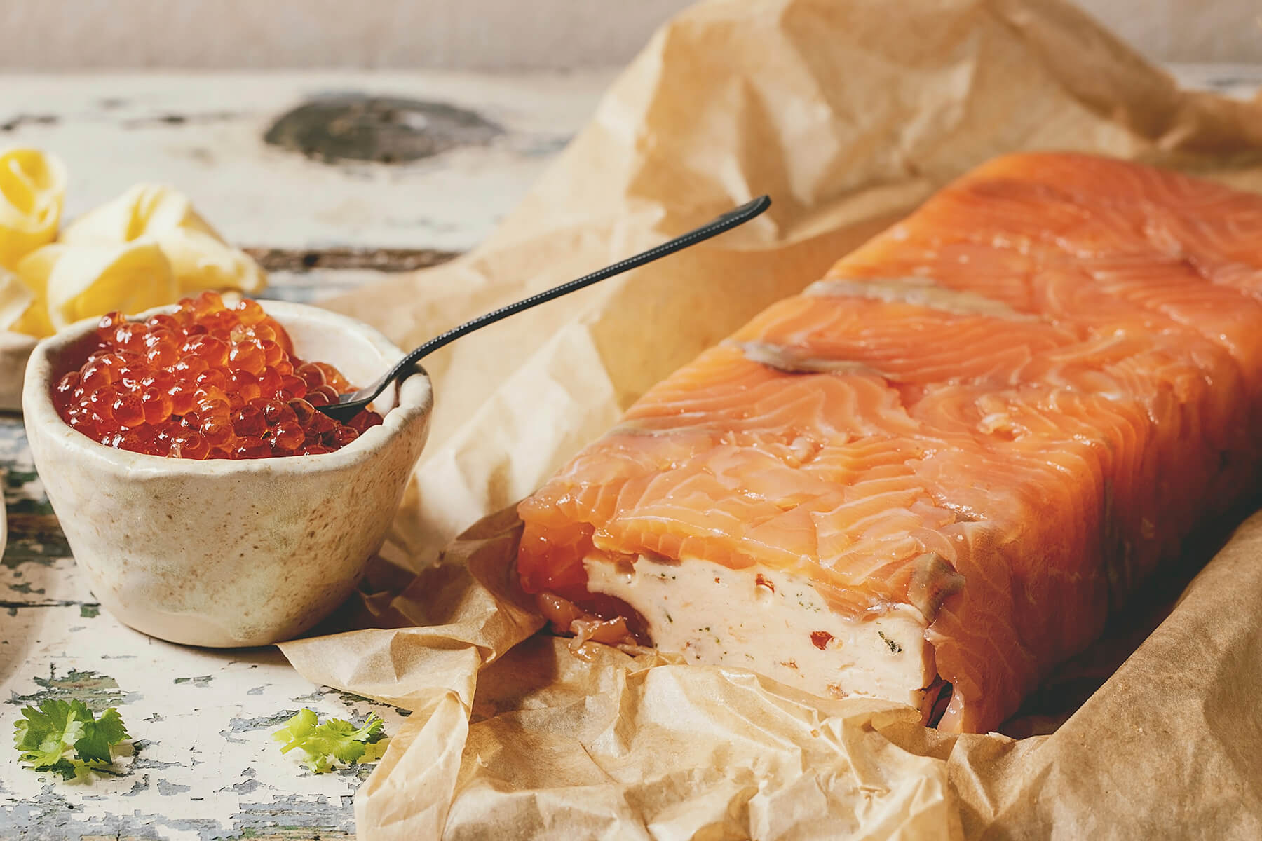 Angeschnittene Lachs-Terrine mit cremiger Frischkäse-Füllung und einer Schale roter Kaviar daneben