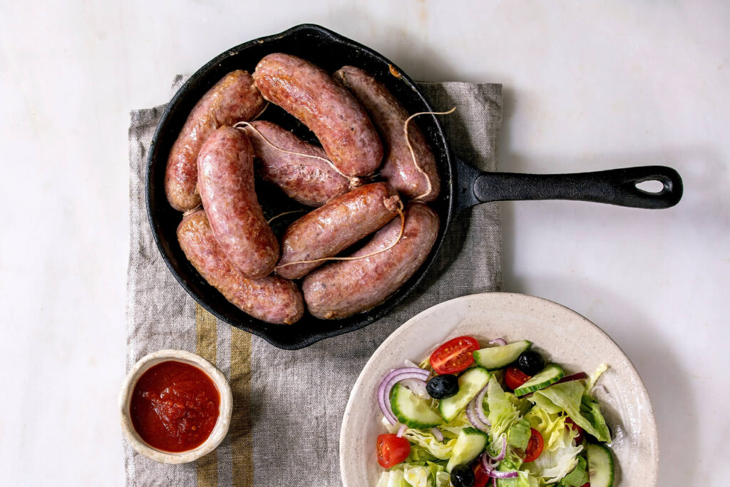 Gegrillte italienische Salsiccia in Gusseisen-Pfanne mit Tomatensauce und Salat