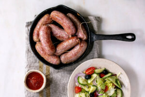 Gegrillte italienische Salsiccia in Gusseisen-Pfanne mit Tomatensauce und Salat