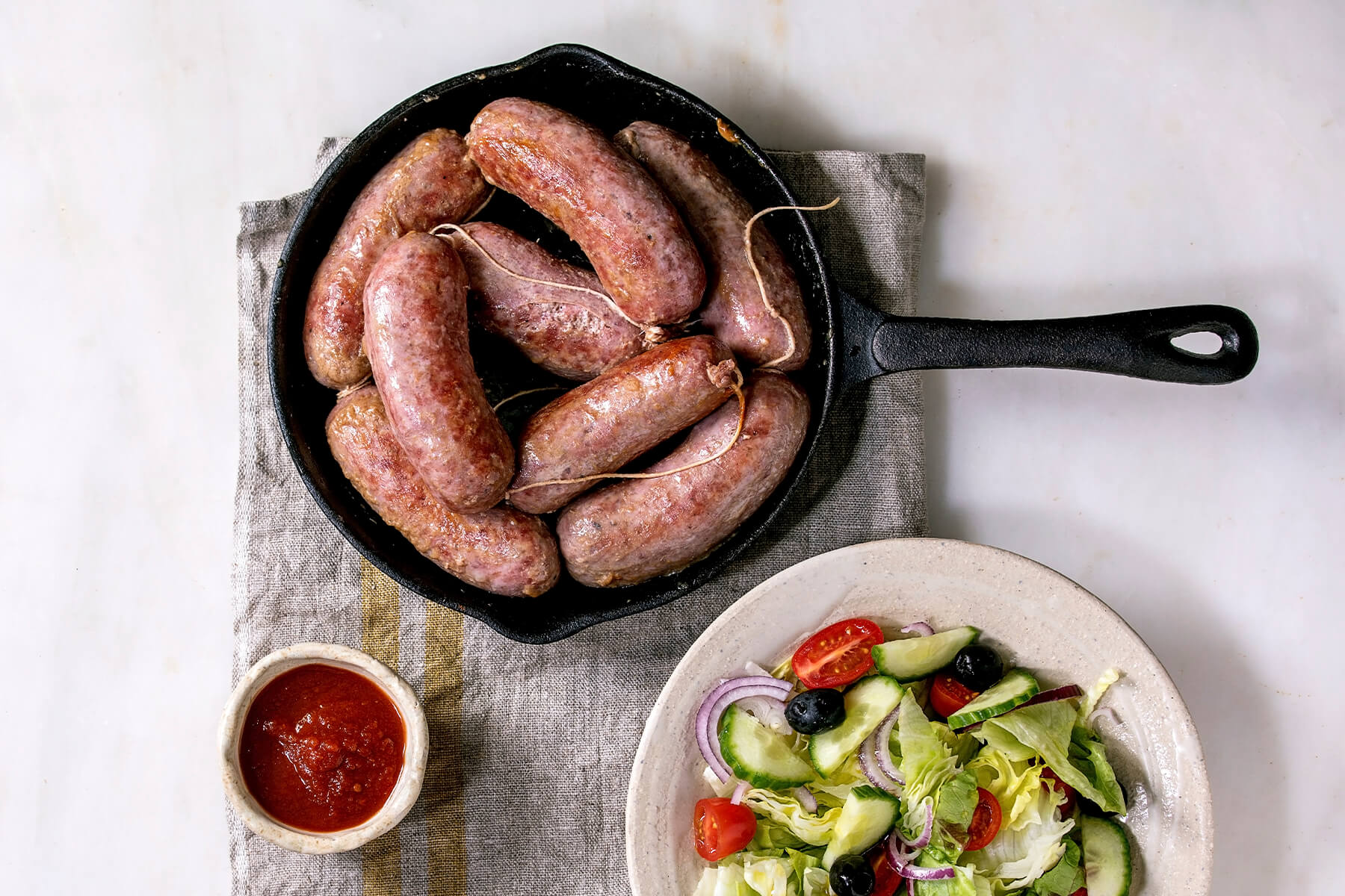 Gegrillte italienische Salsiccia in Gusseisen-Pfanne mit Tomatensauce und Salat