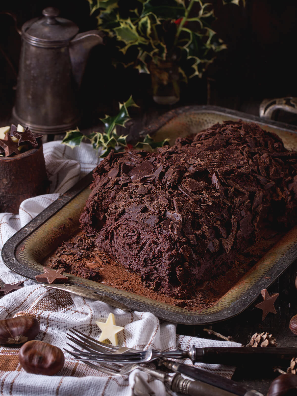 Ganze Bûche de Noël auf einer Platte, dicht mit groben Schokoladensplittern bedeckt und mit Kakao bestäubt