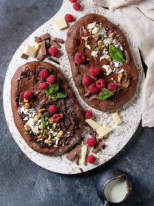 Ovale Schoko-Pizza mit Schoko-Aufstrich, Himbeeren und Walnüssen – rustikales Dessert aus Kakao-Teig