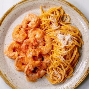 Teller von oben: goldgelbe Eier-Linguine mit fein geriebenem Parmesan neben Garnelen in heller Tomaten-Sahne-Sauce