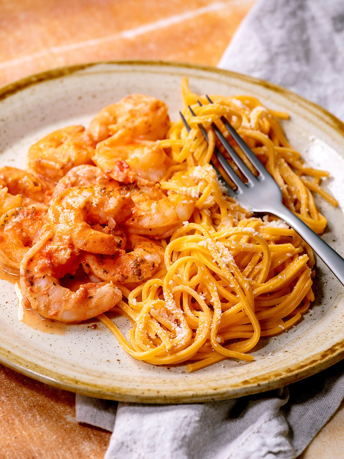 Gabel auf goldgelben Eier-Linguine mit fein geriebenem Parmesan, daneben Garnelen in heller Tomaten-Sahne-Sauce