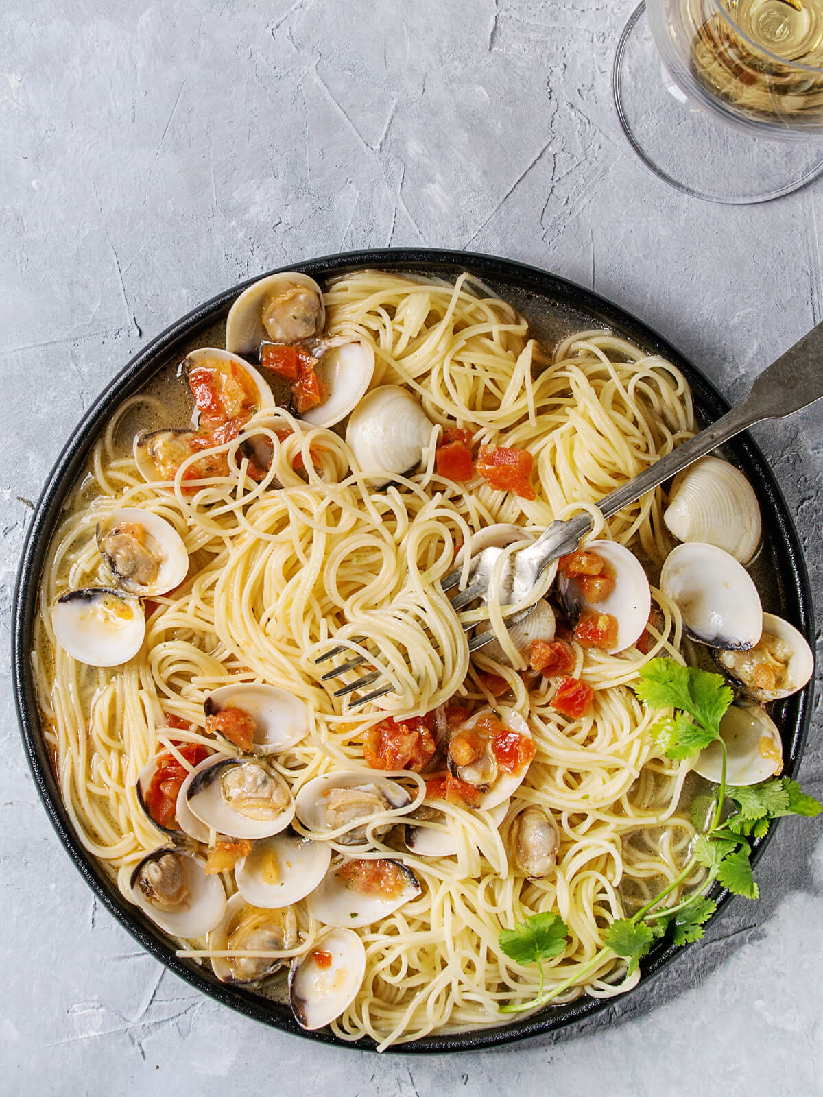 Spaghetti alle Vongole mit geöffneten Venusmuscheln und Tomatenstücken auf dunklem Teller mit Gabel