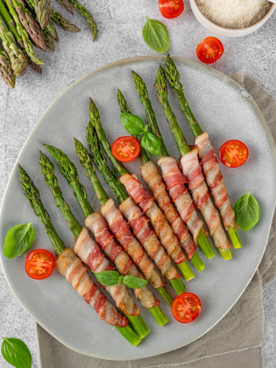 Grüner Spargel im Speckmantel diagonal auf einer grau-blauen Platte angerichtet