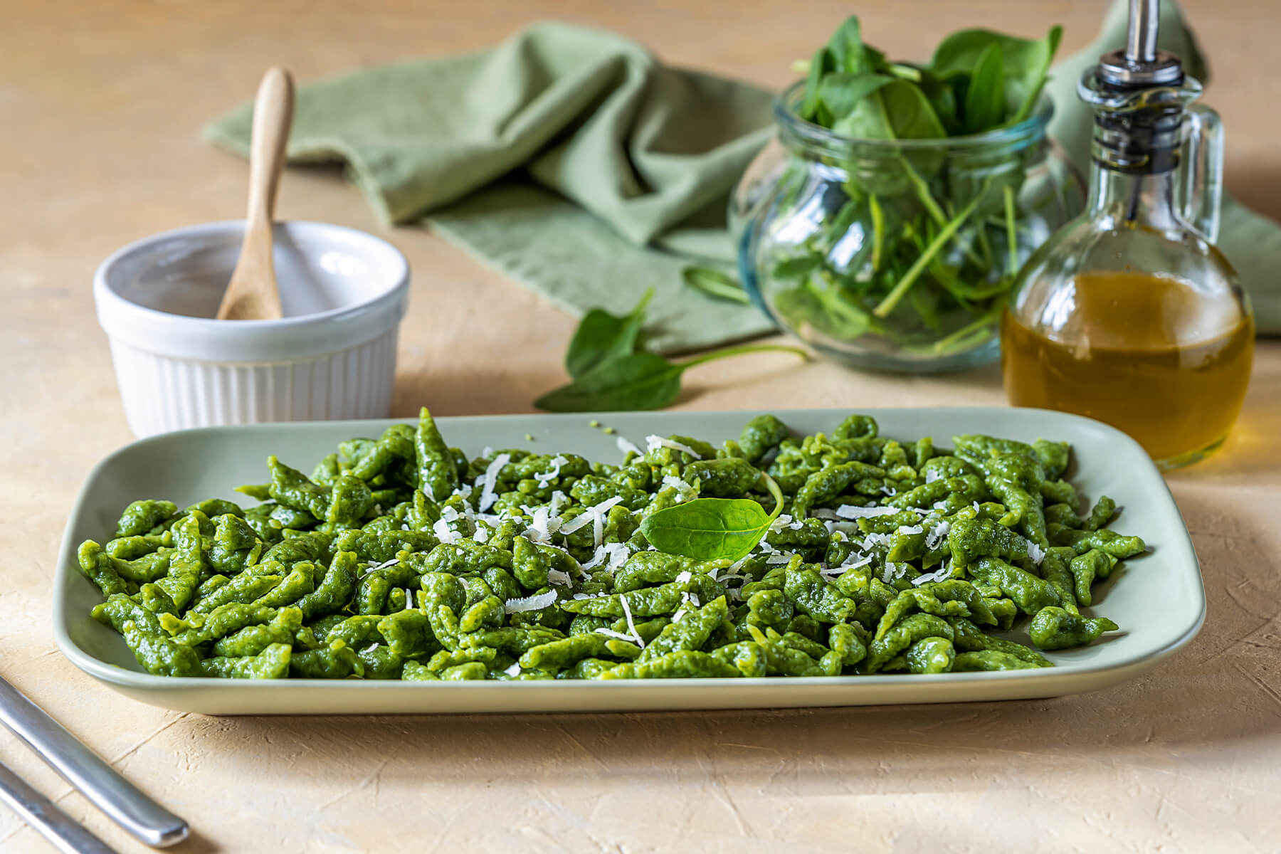Grüne Tiroler Spinat-Spätzle auf einer Platte, bestreut mit geriebenem Parmesan und einem frischen Spinatblatt