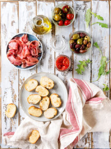 Tapas-Brett mit gerösteten Baguette-Scheiben, Serrano, Oliven und eingelegten Tomaten