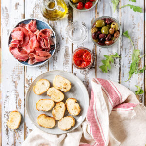 Tapas-Brett mit gerösteten Baguette-Scheiben, Serrano, Oliven und eingelegten Tomaten